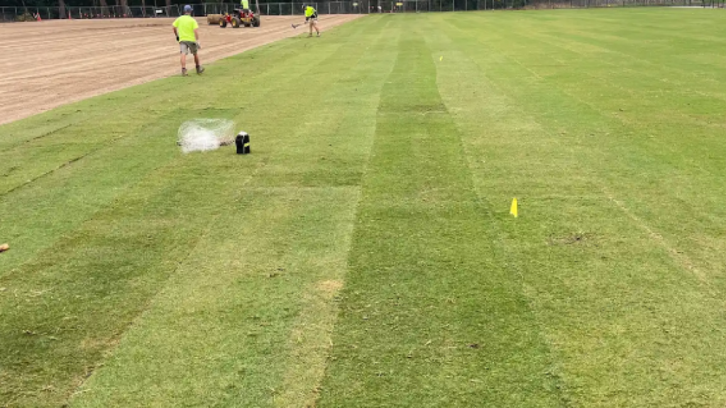 Striped sports field with workers and sprinkler