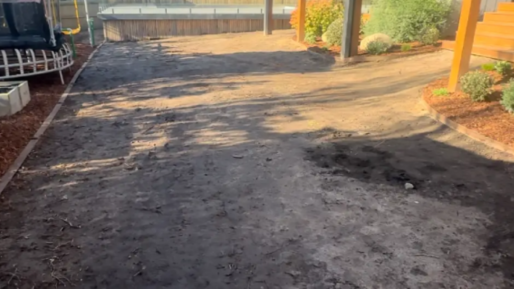 Mt Eliza backyard before TifTuf Bermuda turf installation, showing the sandy soil base and sloped terrain that required levelling and preparation.