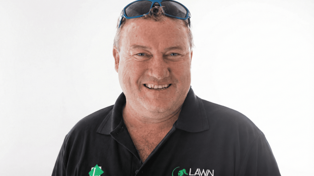 Smiling man in a black lawn care company polo shirt with blue sunglasses pushed up on his head.