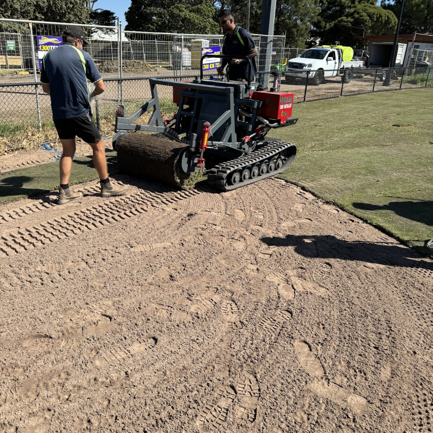Machine laying turf beside an existing sports field surface