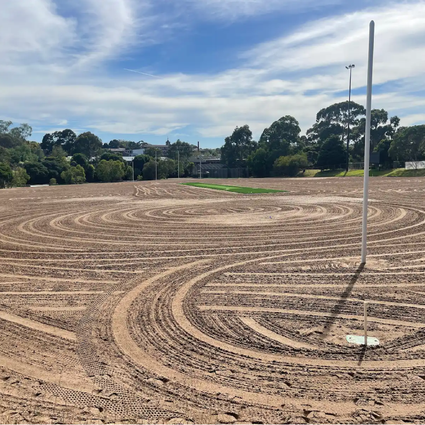 Prepared dirt field with spiral cultivation pattern and floodlight pole.