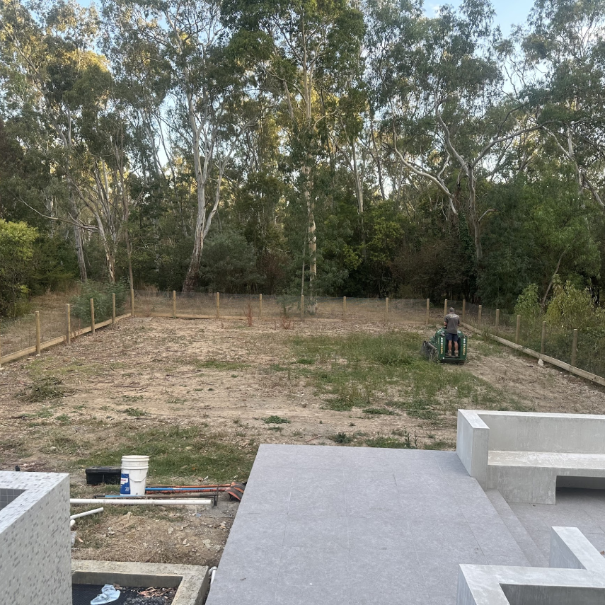 Backyard before landscaping with bare ground and bushland backdrop
