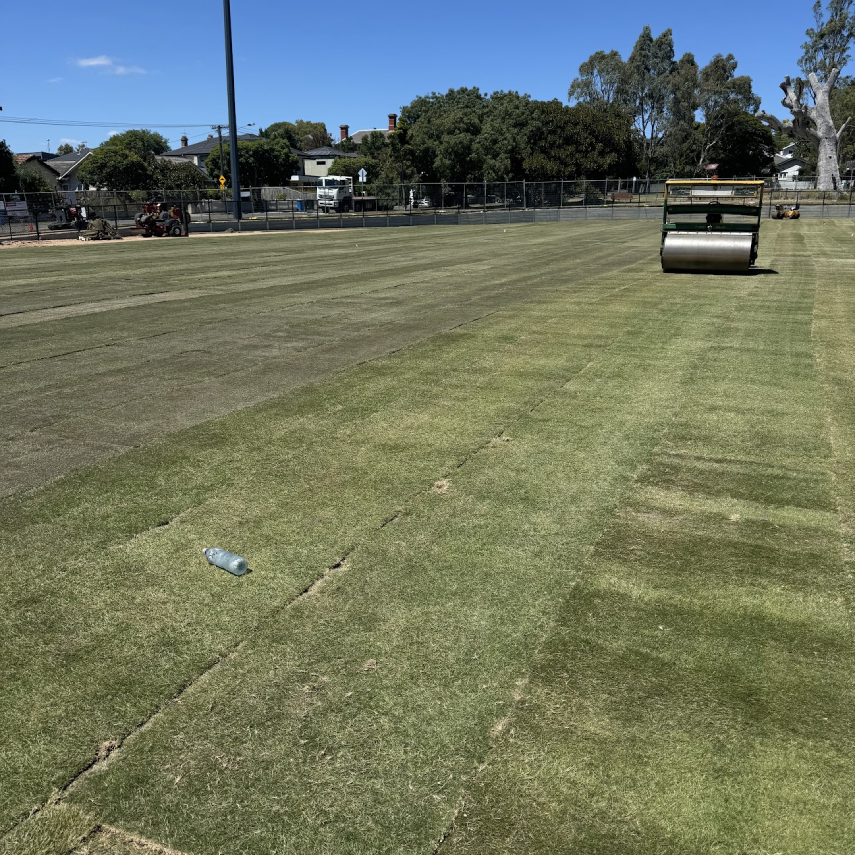 Field with turf seams and compaction equipment during installation.