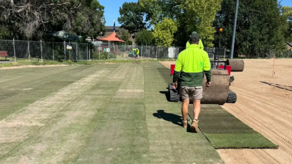 Worker laying turf on a sports field