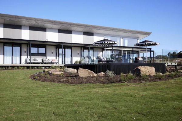 Modern clubhouse with outdoor seating and umbrellas overlooking a newly laid lawn and landscaped garden beds.