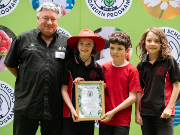 Lilydale Instant Lawn representative presenting a framed certificate to three primary school students at a School Garden Program event