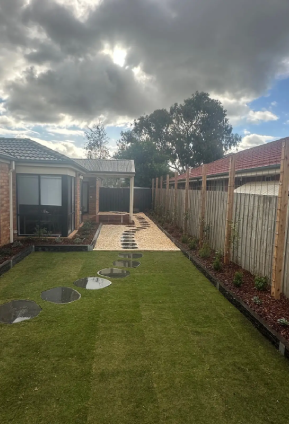 Backyard with newly laid lawn and circular stepping stones leading to a gravel path, bordered by garden beds and a timber fence.